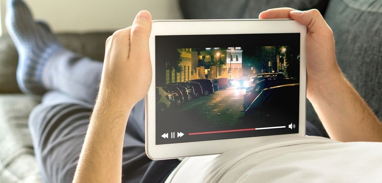 Person reclining and holding a tablet that is playing a video.