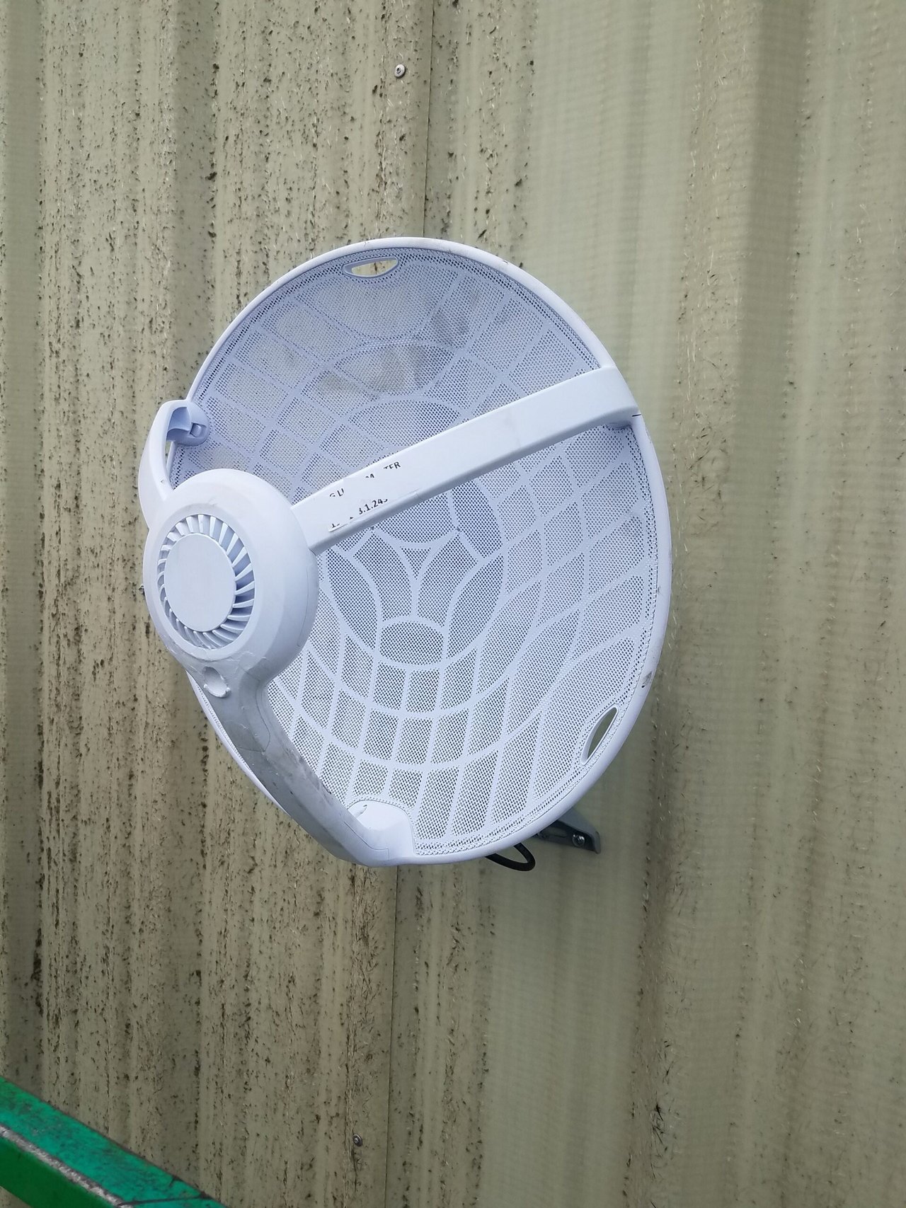 White mesh parabolic wireless antenna mounted on a corrugated metal wall.