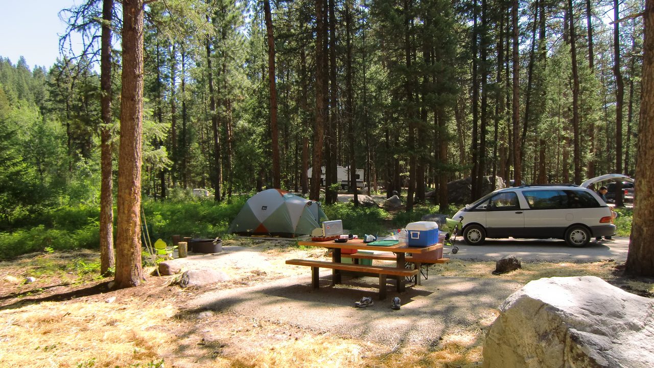 Tent, picnic table, and fire ring at a wooded campground site.