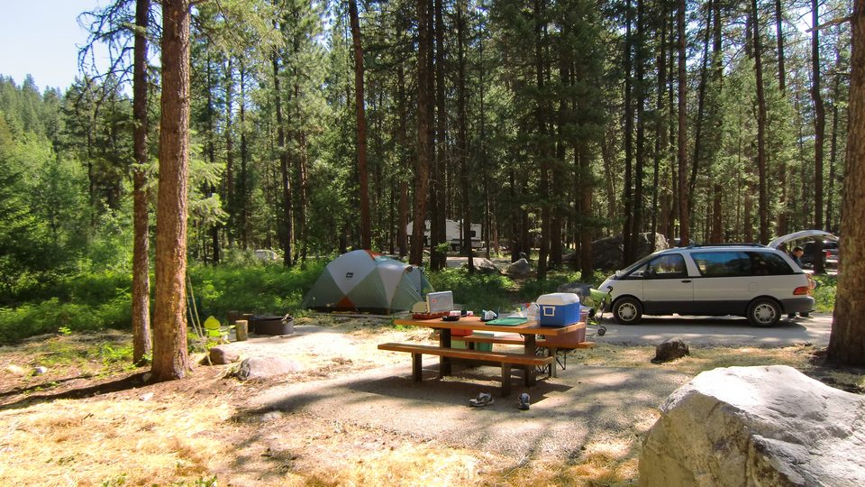 Tent, picnic table, and fire ring at a wooded campground site.