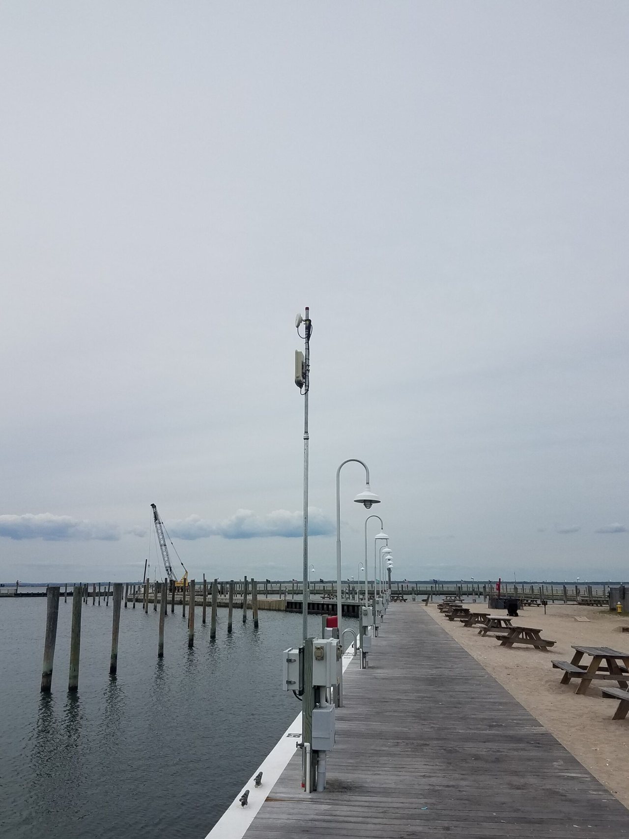 Galvanized metal pole on a wooden marina boardwalk with a rectangular outdoor antenna near the top and grey weatherproof enclosures at the base.