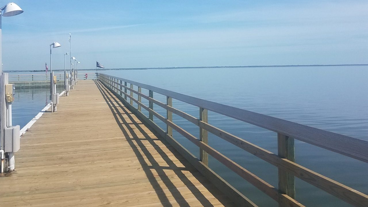 Wooden marina dock with light poles and weatherproof equipment mounted along the walkway over calm water.