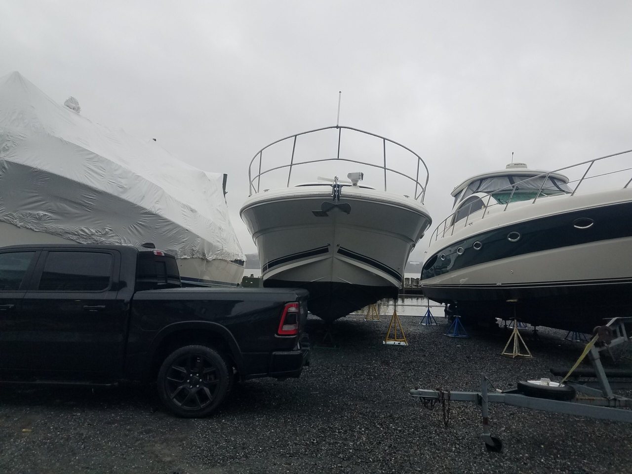 Boats on stands in a marina dry-storage yard, including one shrink-wrapped hull