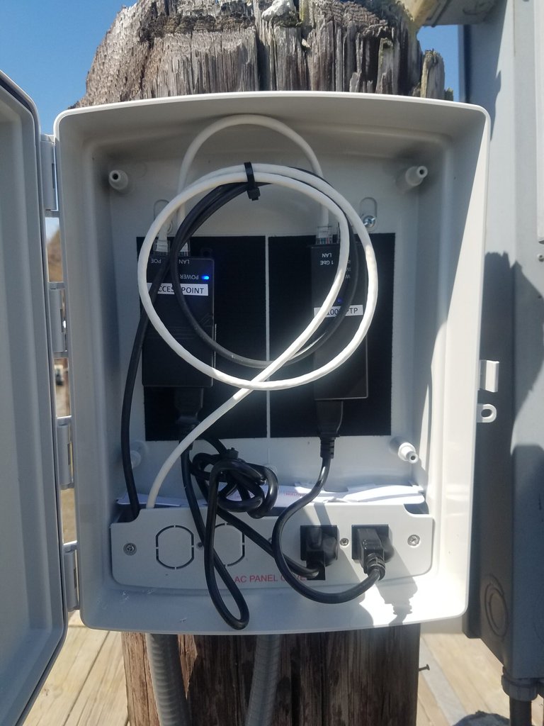Open weatherproof enclosure with PoE injectors and power connections mounted on an outdoor wooden piling